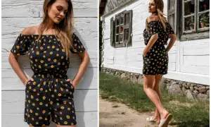 Krótki kombinezon hiszpanka w słoneczniki, idealny na letnie dni. Modelka prezentuje go na tle drewnianej chatki.