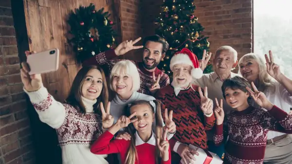 Wesoła rodzina robi sobie świąteczne stylizacje rodzinne selfie przy choince. Wszyscy pozdrawiają gestem pokoju.