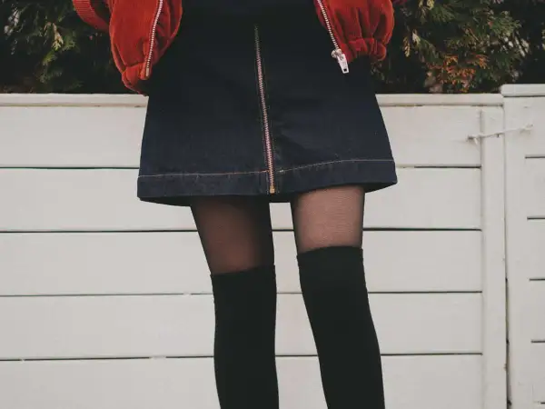 Stylowy outfit z dżinsową spódniczką, czarnymi zakolanówkami i pomarańczową kurtką.