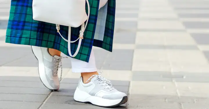 Stylowe białe sneakersy damskie idealnie komponują się z białą stylizacją i zielono-niebieską kraciastą marynarką.